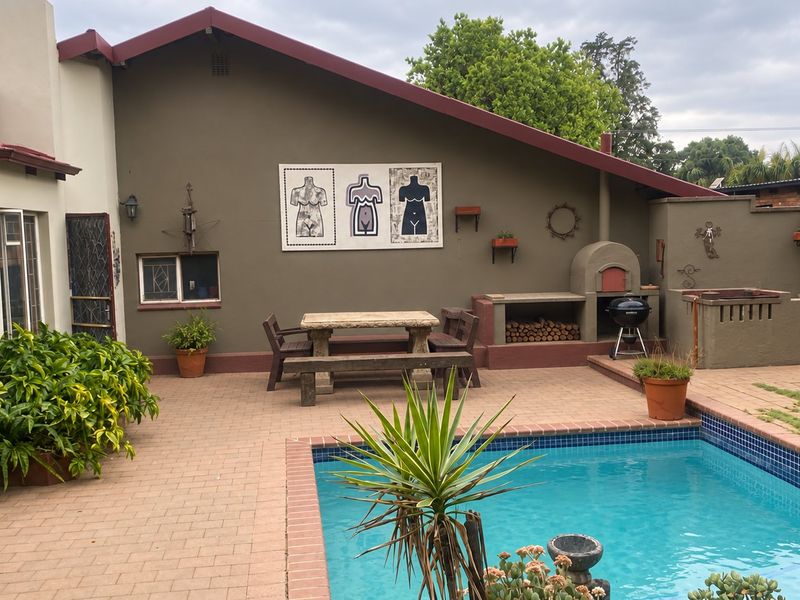 Outdoor entertainment area featuring a swimming pool, brick paved patio, and a built-in pizza oven against a rendered wall.