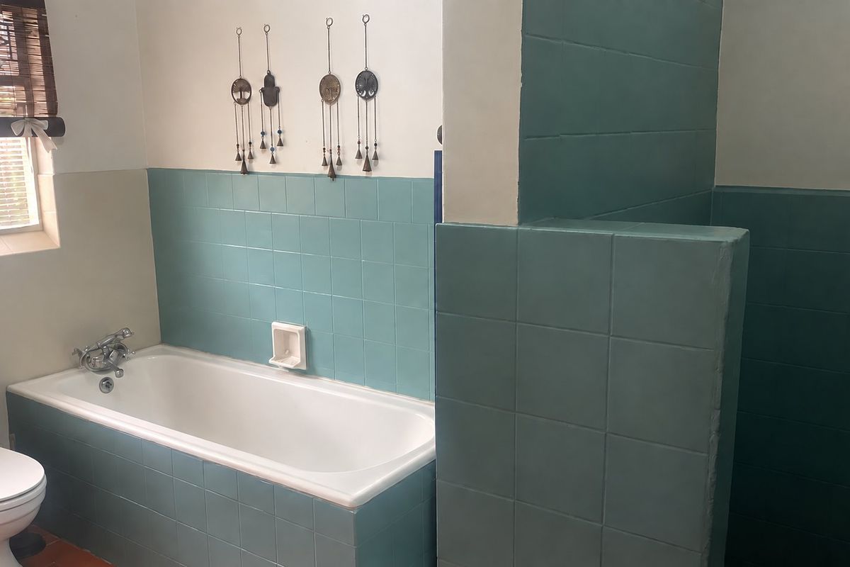 A functional bathroom featuring a built-in bathtub, tiled partition wall, and standard sanitary fixtures with teal ceramic wall tiling.