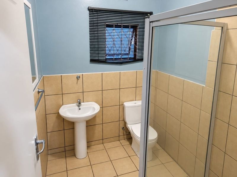 A clean and functional bathroom featuring a pedestal basin, toilet, and a glass-enclosed shower with neutral wall and floor tiling.