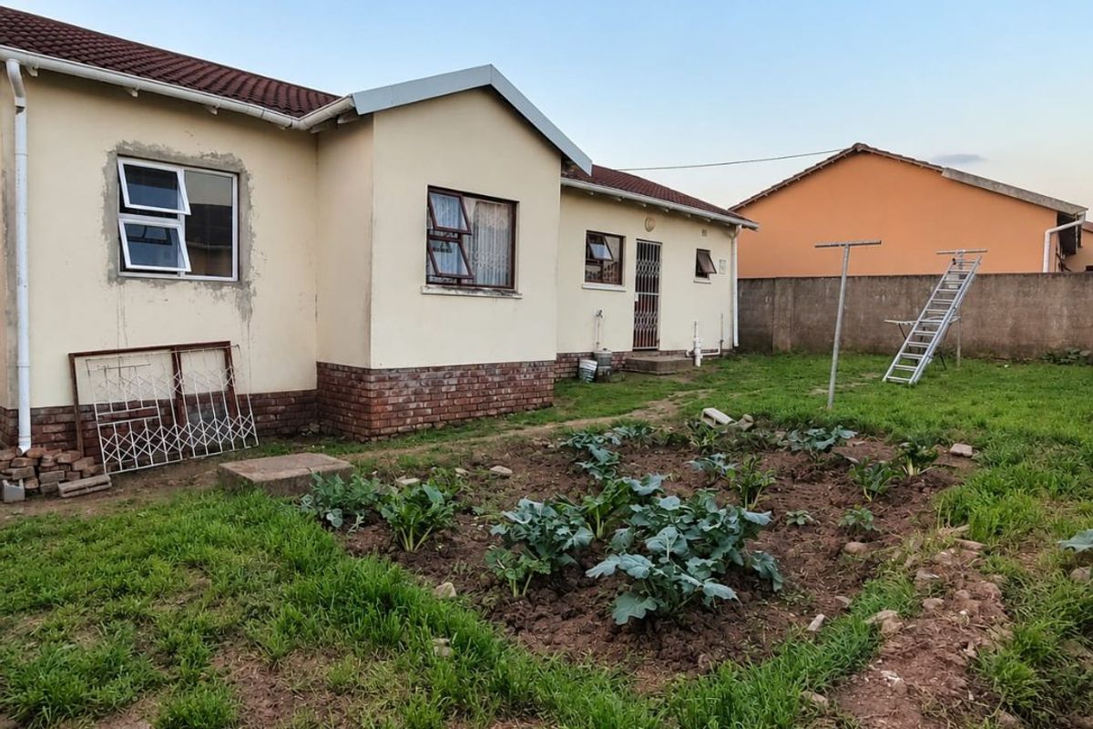 Rear view of the house featuring a tiled roof, brick plinth, and a garden area with a perimeter wall.