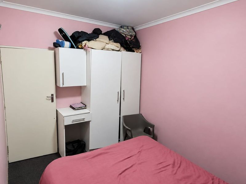 A bedroom featuring built-in cabinetry including a wardrobe and desk, finished with pink walls and dark carpeting.