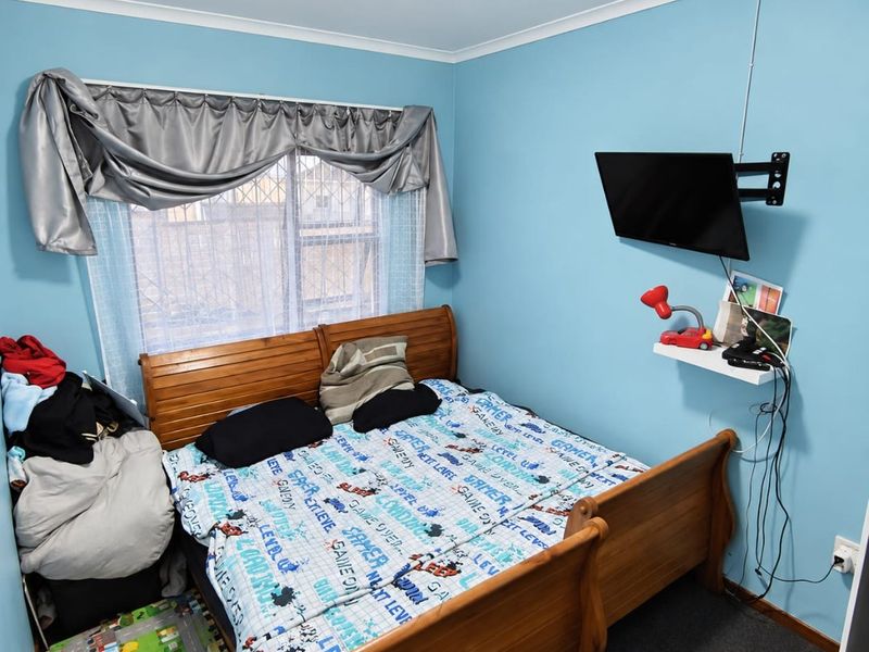 A bedroom featuring blue walls, a window with security bars, and a wall-mounted television bracket.