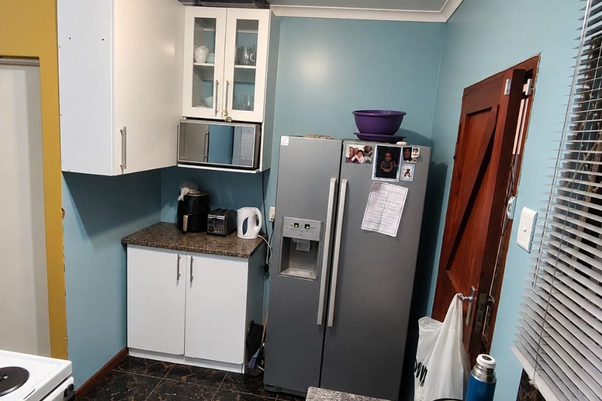A functional kitchen featuring white cabinetry, laminate countertops, and dark tiled flooring, providing a practical workspace with integrated microwave and ample storage.