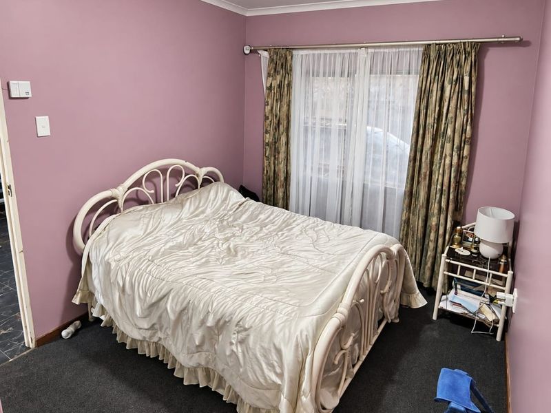 A bedroom featuring dark carpeting, mauve-toned walls, and a window dressed with curtains.