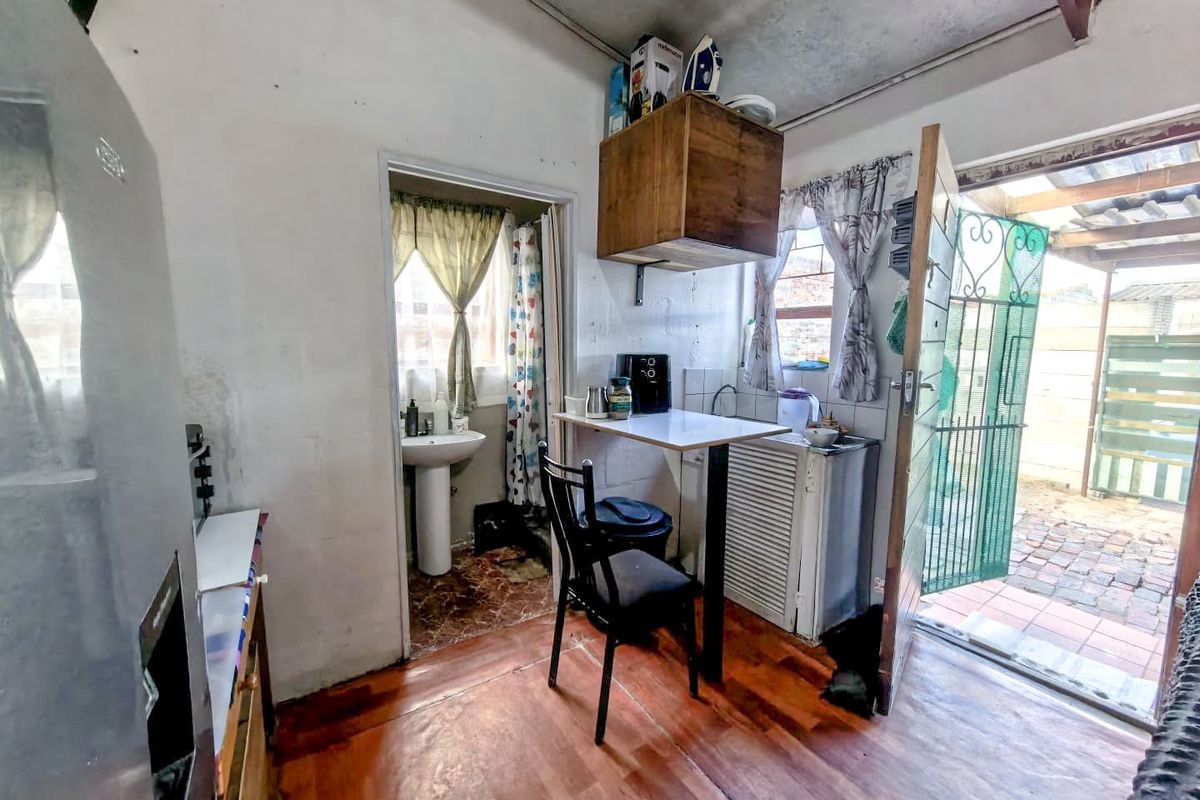 A small, dated kitchen area featuring timber flooring, a pedestal sink in the adjacent space, and direct access to an outdoor area via a security gate.