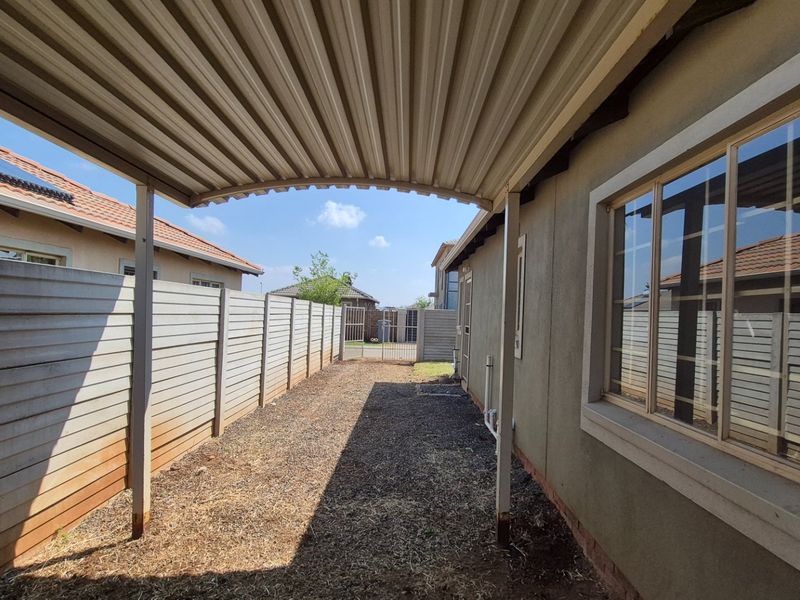 Side exterior area featuring a corrugated metal carport, precast concrete boundary wall, and aluminum window frames along the side of the house.