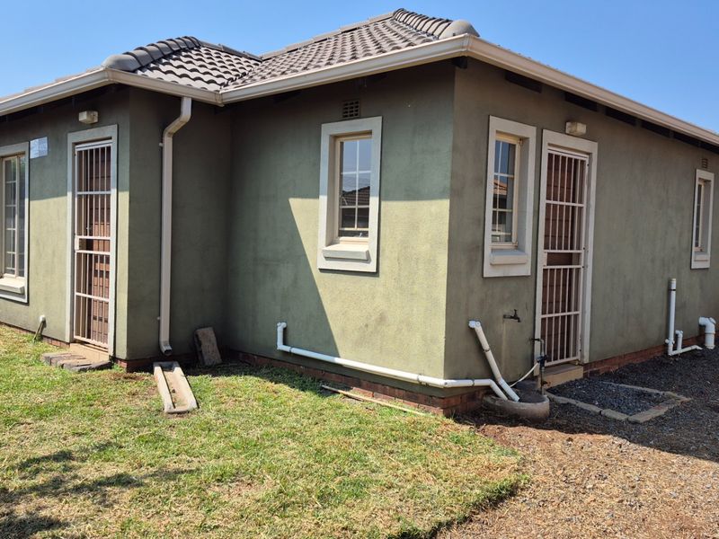 Rear exterior view of the house featuring plastered walls, tiled roof, security gates, and exposed external plumbing infrastructure.