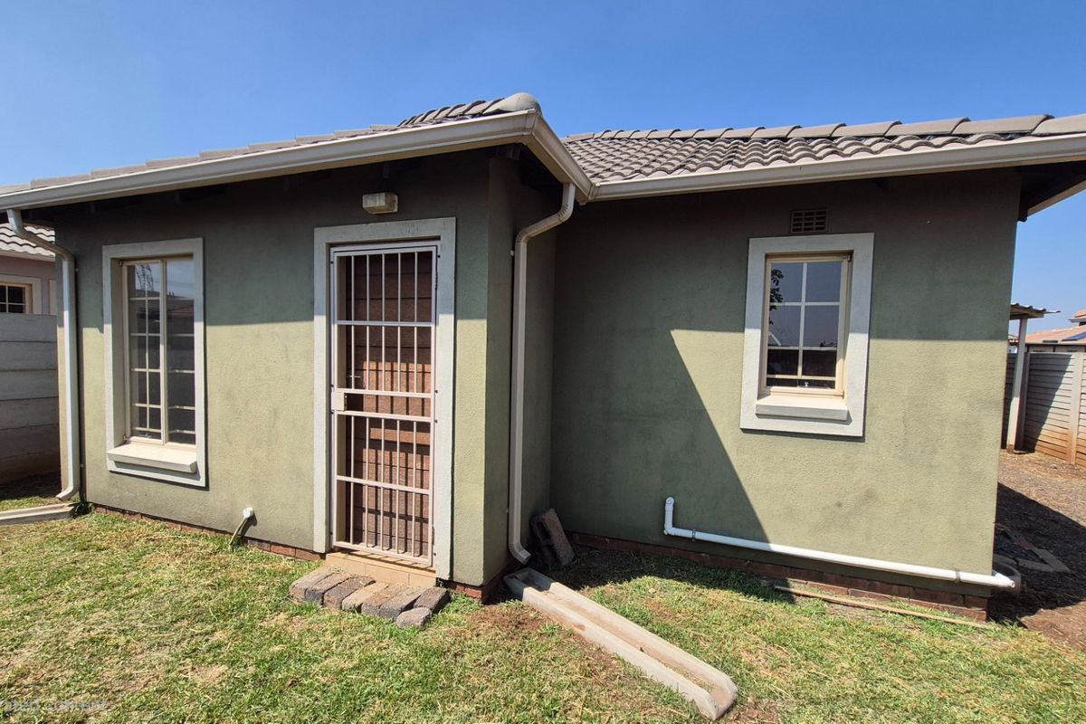 Rear exterior view of the house featuring a tiled roof, security gate, and precast concrete boundary walling.