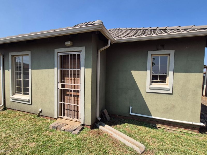 Rear exterior view of the house featuring a tiled roof, security gate, and precast concrete boundary walling.