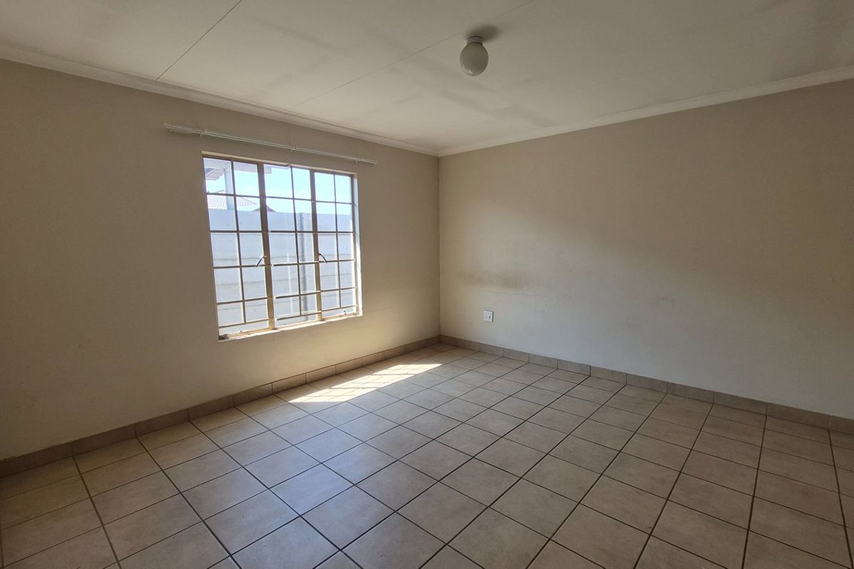 An empty bedroom featuring neutral tiled flooring, a window with security bars, and a simple ceiling light fixture, ready for personalization.