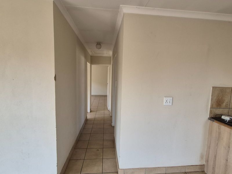 A functional hallway connecting living spaces, featuring tiled flooring and neutral walls, leading towards additional rooms in the property.