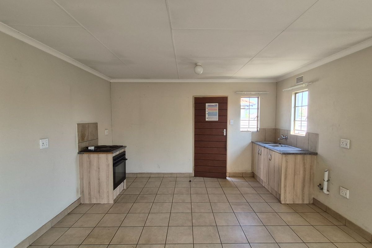 A functional, empty kitchen featuring tiled flooring, built-in cabinetry, a stove with oven, and a sink, offering a blank canvas for potential updates.