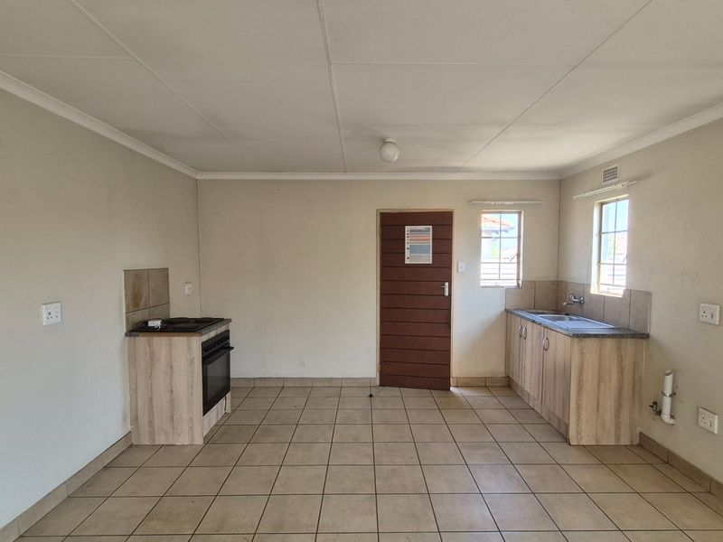 A functional, empty kitchen featuring tiled flooring, built-in cabinetry, a stove with oven, and a sink, offering a blank canvas for potential updates.