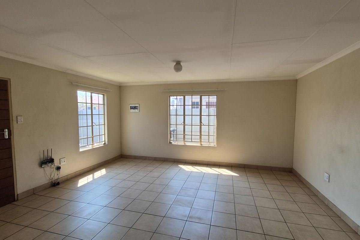 An empty living room featuring tiled flooring, security bars on the windows, and neutral wall finishes, offering a blank canvas for interior design.