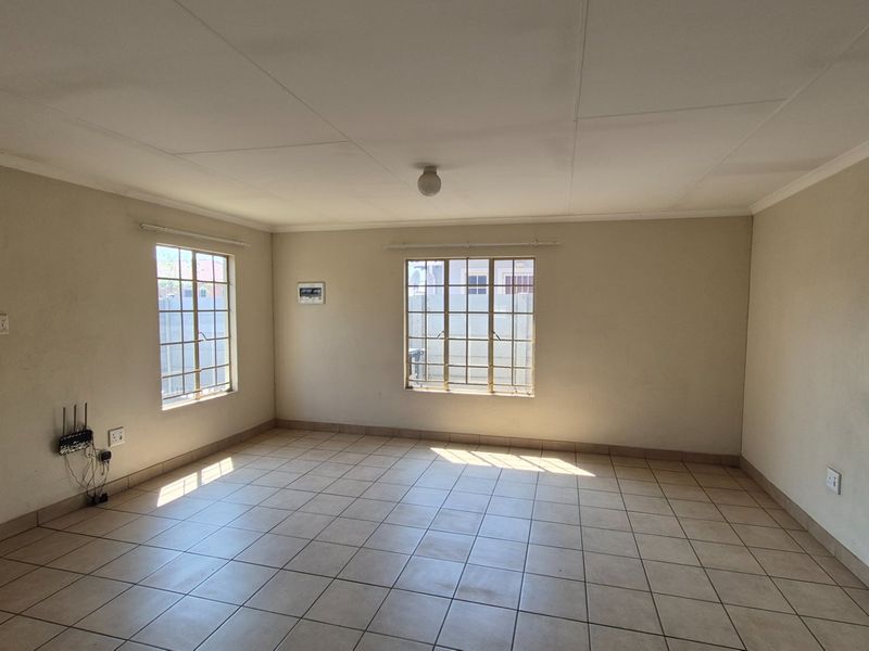 An empty living room featuring tiled flooring, security bars on the windows, and neutral wall finishes, offering a blank canvas for interior design.