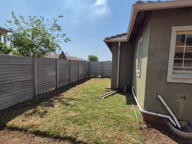 A view of the rear exterior area featuring a precast concrete boundary wall, lawn, and exposed external plumbing along the house wall.