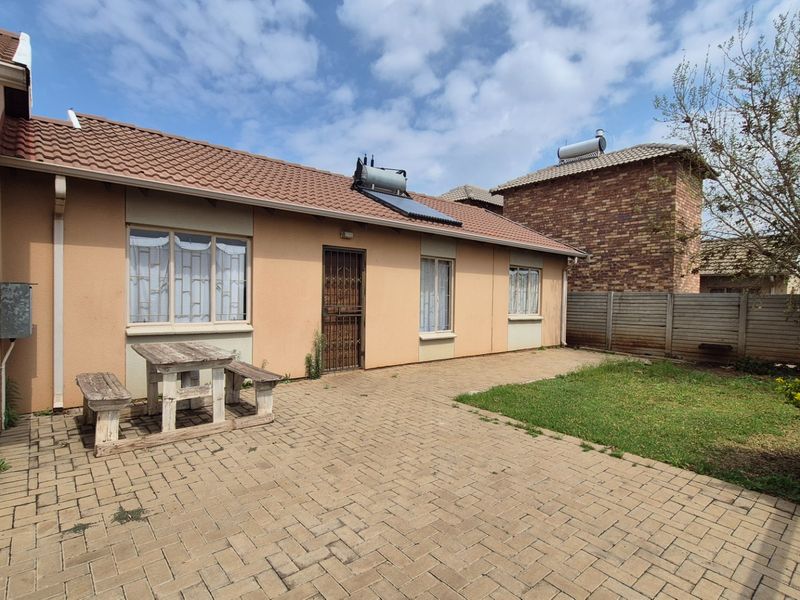 Rear exterior view of the house featuring a paved patio area, solar water heating system, and a small garden with perimeter walling.