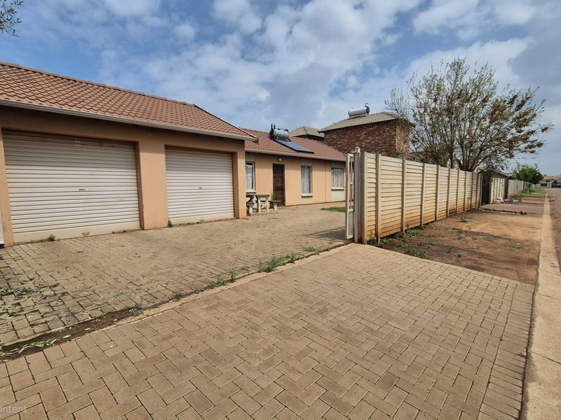 Front exterior view of a single-story house featuring a double garage, paved driveway, and solar water heating system.