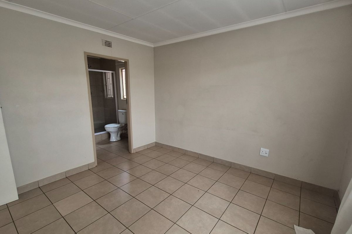 A clean, empty bedroom featuring neutral tiled flooring and direct access to an en-suite bathroom.