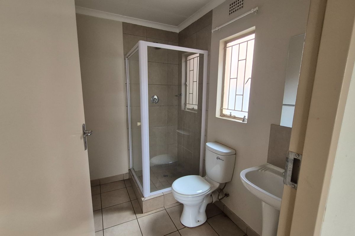 A functional bathroom featuring a shower enclosure, pedestal basin, and toilet with neutral tiled flooring and walls.