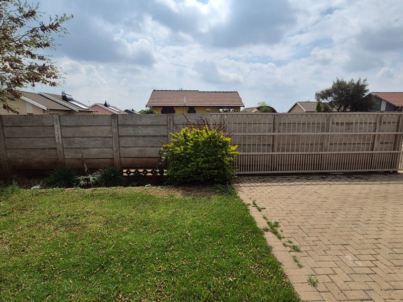 Front exterior view featuring a paved driveway, sliding gate, and precast concrete boundary wall with a small lawn area.