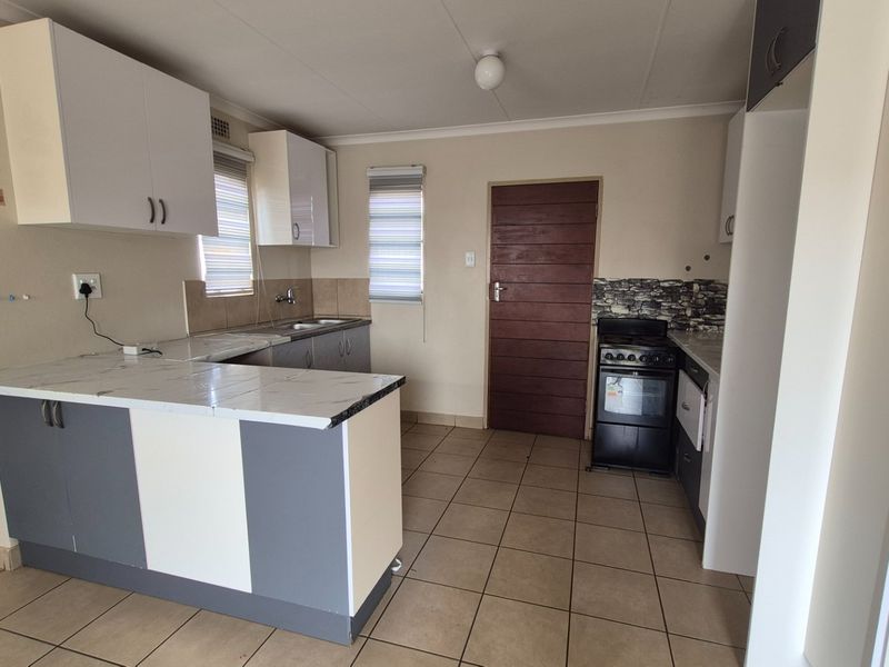 A functional kitchen featuring two-tone cabinetry, marble-look laminate countertops, tiled flooring, and a freestanding stove with a tiled splashback.