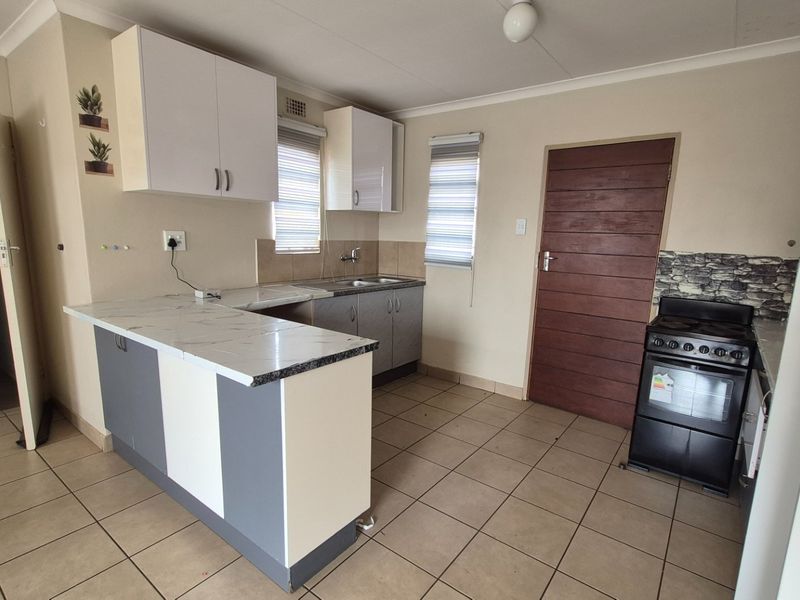 A clean, functional kitchen featuring modern two-tone cabinetry, laminate countertops, tiled flooring, and a freestanding stove.