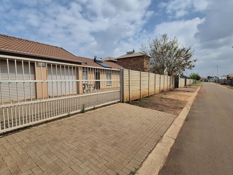 Street view of a residential property featuring a paved driveway, sliding security gate, and precast concrete boundary wall with a solar water heater installed.
