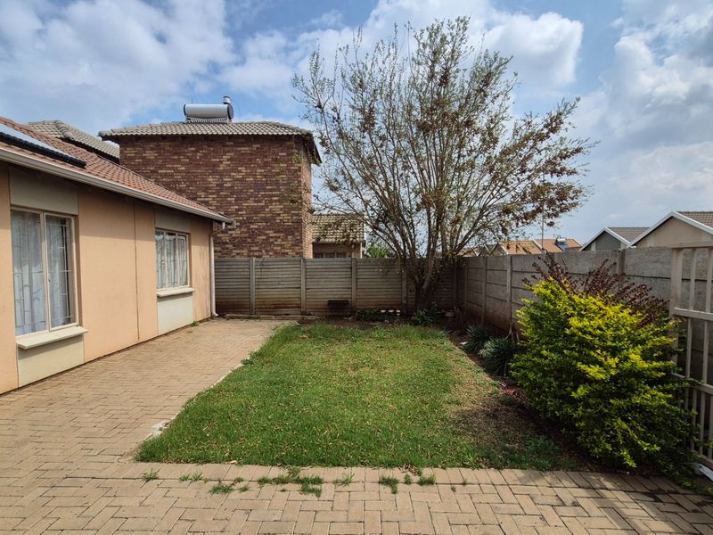 Rear exterior view featuring a paved patio area, small lawn, and precast concrete boundary wall with a solar water heater installed on the roof.