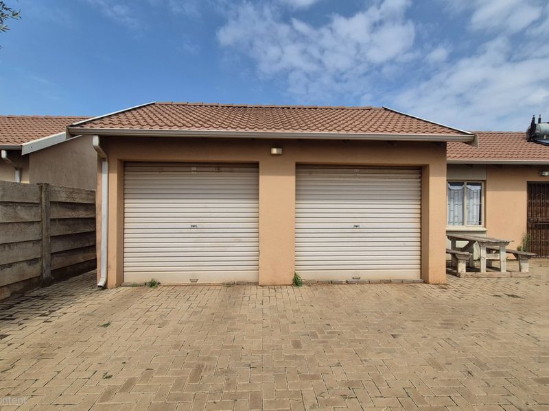 A double garage with roller shutter doors, featuring a paved driveway and a solar water heating system on the tiled roof.