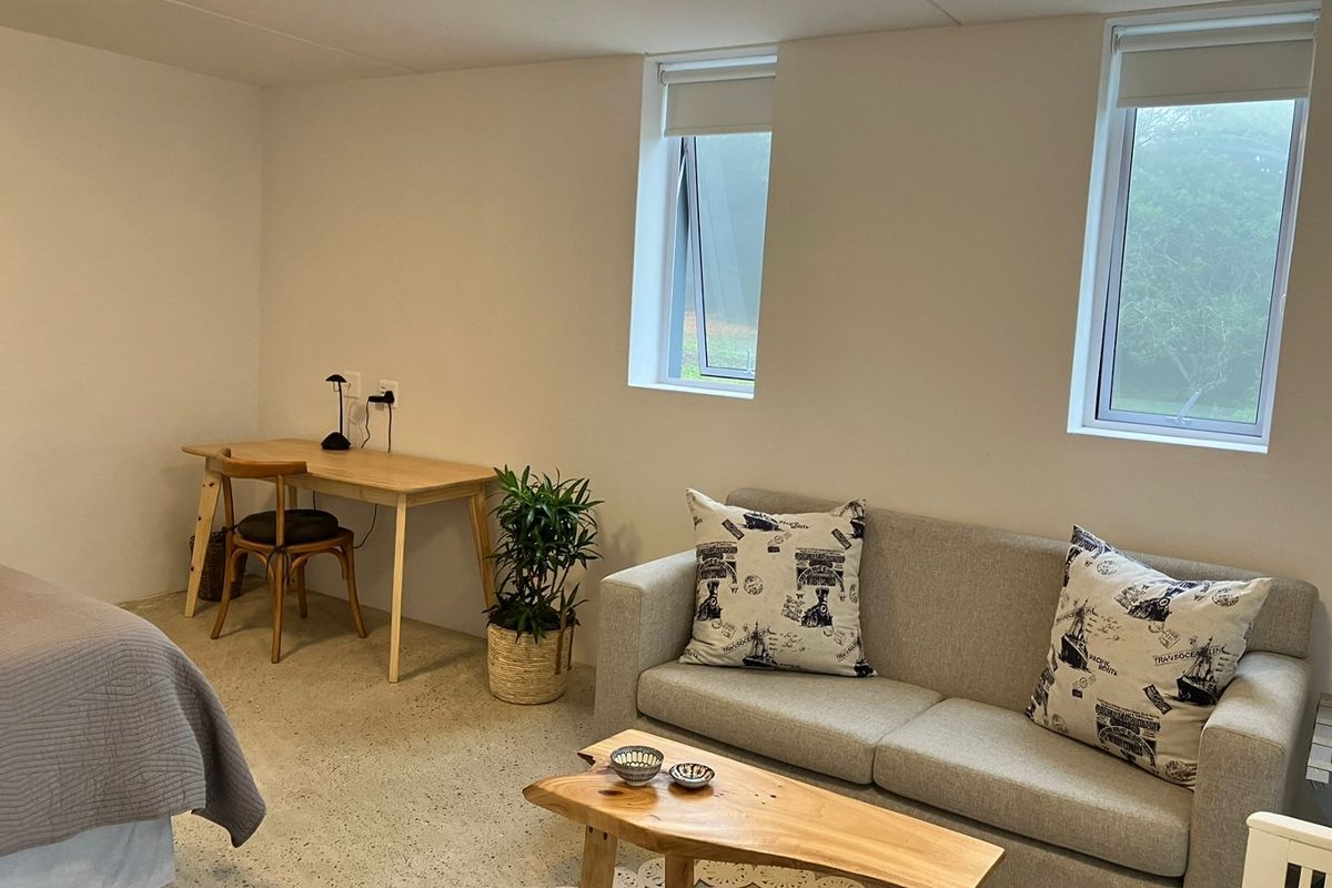 A well-lit bedroom featuring polished concrete flooring and dual casement windows with roller blinds, offering a clean and modern aesthetic.