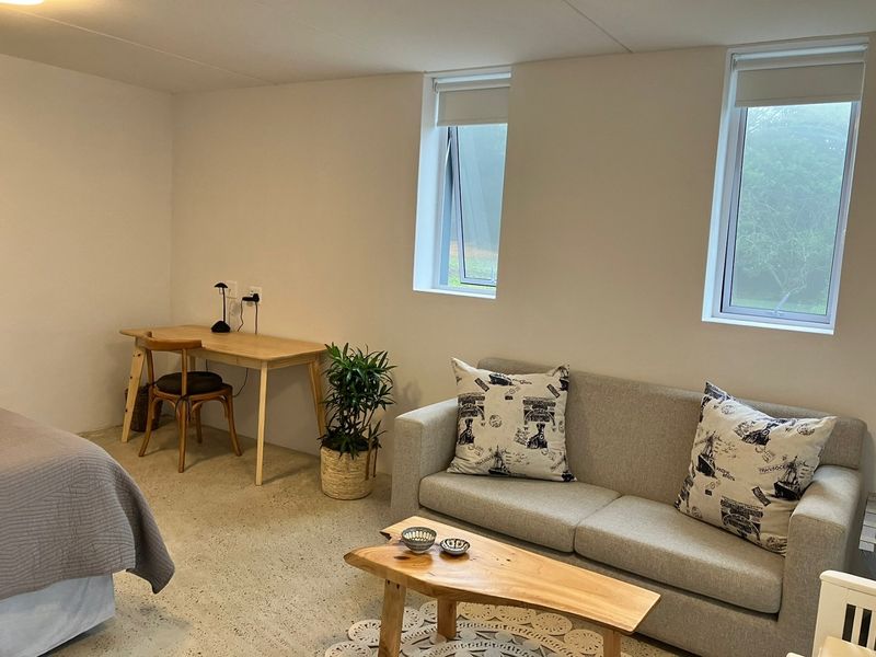 A well-lit bedroom featuring polished concrete flooring and dual casement windows with roller blinds, offering a clean and modern aesthetic.