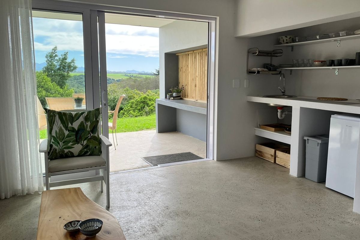 Open-plan living area featuring polished concrete floors, a compact kitchenette, and seamless access to a covered patio with scenic landscape views.