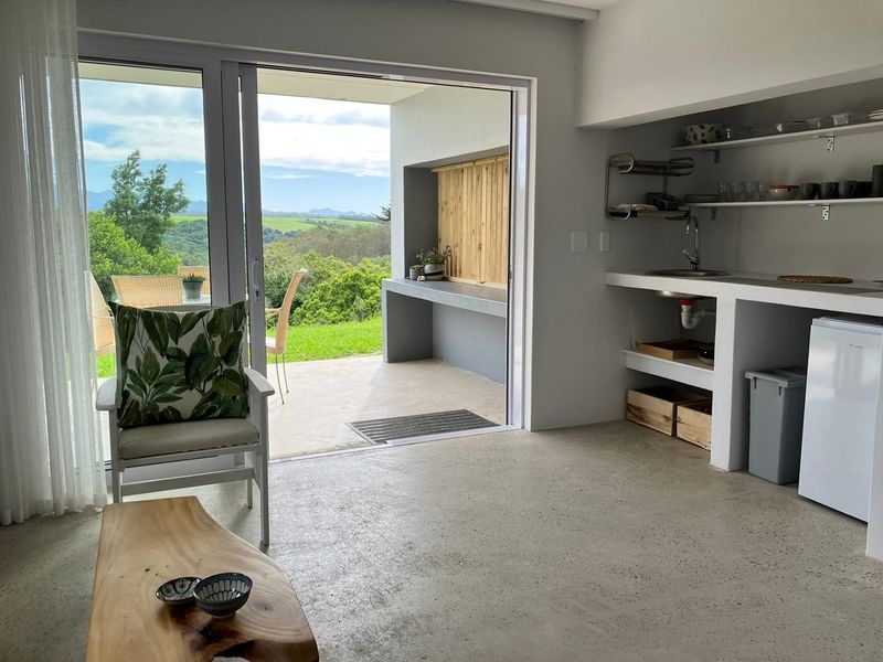 Open-plan living area featuring polished concrete floors, a compact kitchenette, and seamless access to a covered patio with scenic landscape views.