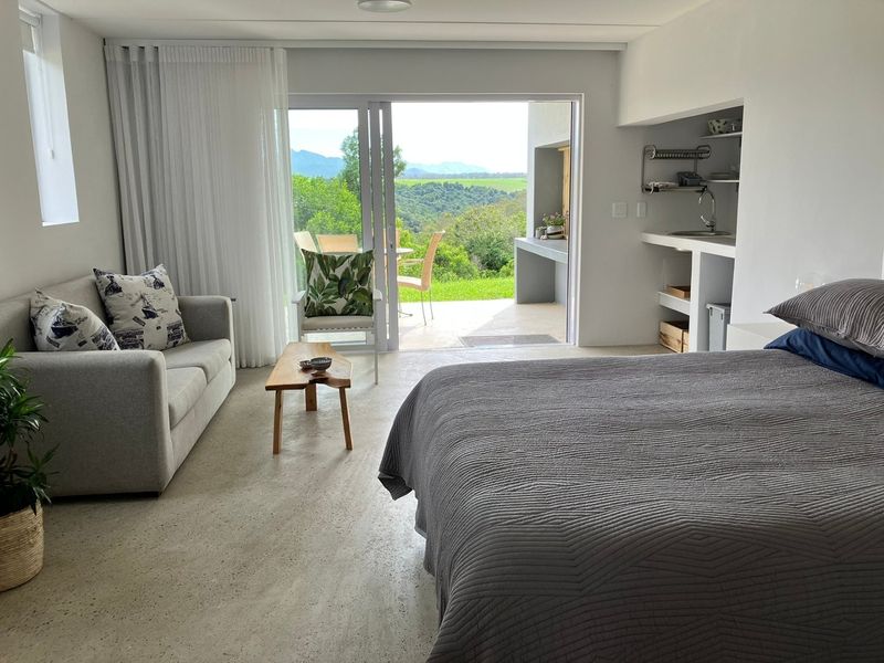 Open-plan studio apartment featuring polished concrete floors, a compact kitchenette, and large sliding doors opening to a scenic patio area.