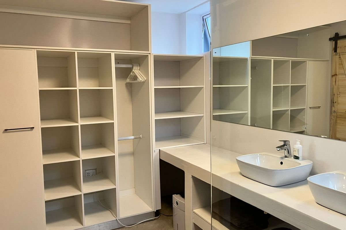 Modern bathroom featuring a concrete double vanity with vessel sinks, large wall mirror, and extensive built-in storage cabinetry.