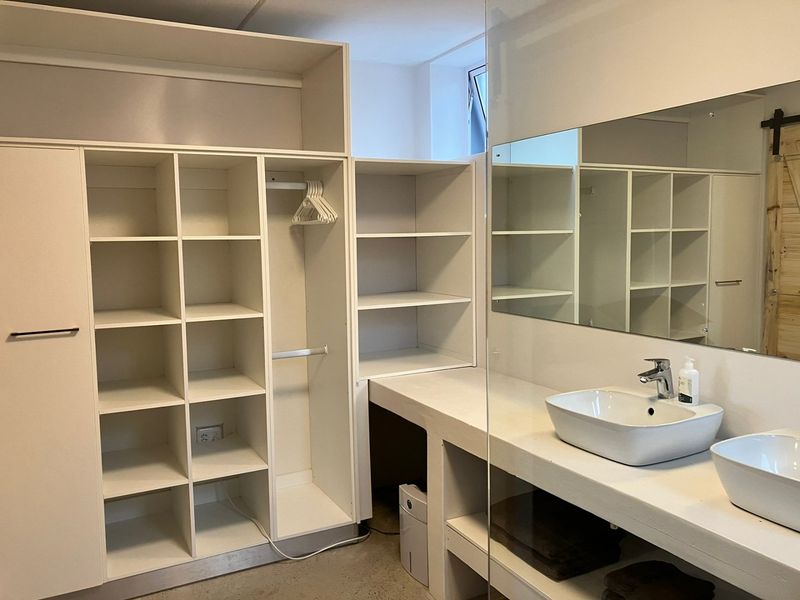 Modern bathroom featuring a concrete double vanity with vessel sinks, large wall mirror, and extensive built-in storage cabinetry.