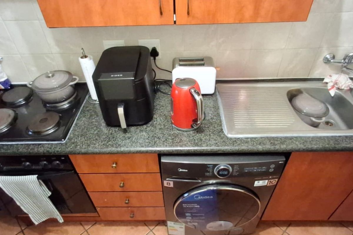 A functional kitchen area featuring a granite countertop, integrated electric hob, built-in oven, and a stainless steel double sink with tiled backsplash.