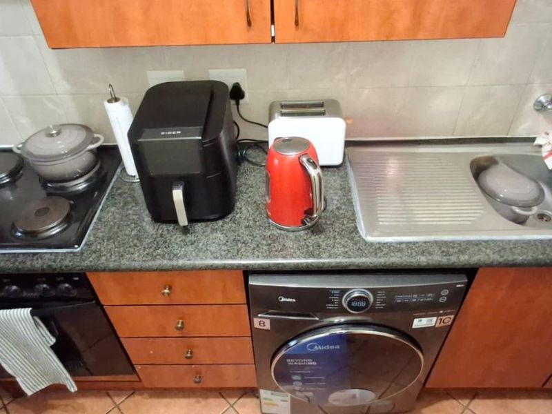 A functional kitchen area featuring a granite countertop, integrated electric hob, built-in oven, and a stainless steel double sink with tiled backsplash.