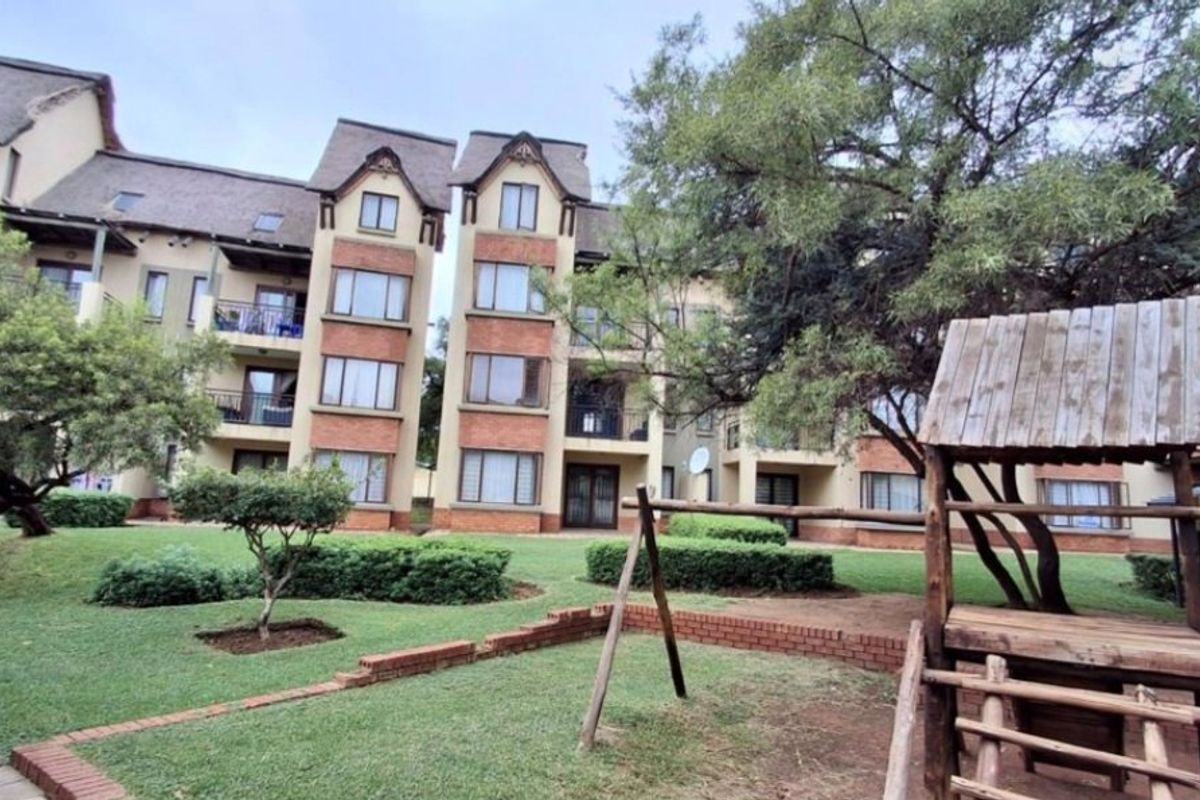 View of the apartment complex rear facade featuring brick construction, thatched roofing, and well-maintained communal garden areas with established trees.