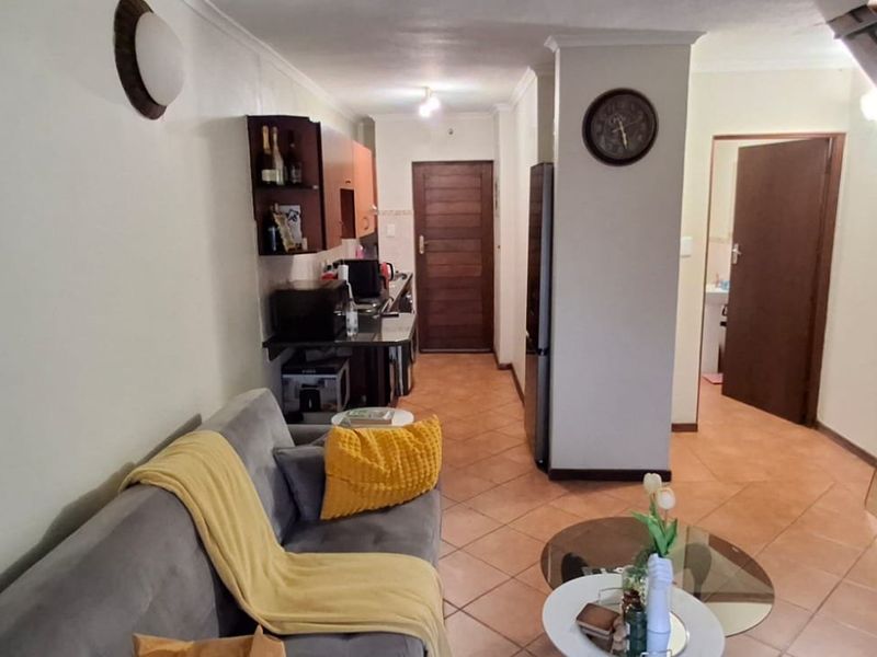 An open-plan living area featuring tiled flooring and a staircase, seamlessly connecting to a compact kitchen space.