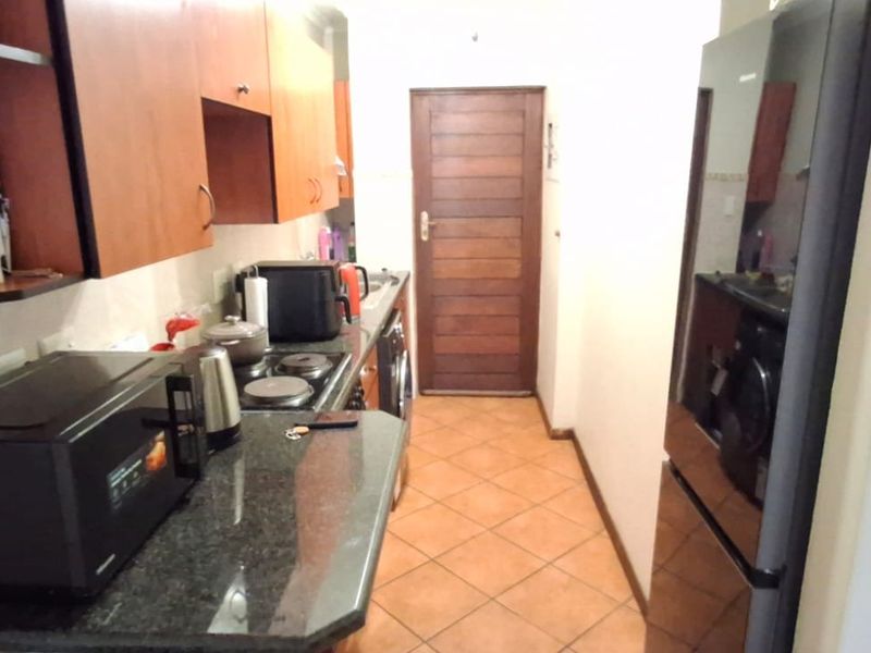 A compact kitchen featuring granite countertops, wooden cabinetry, an electric hob, and tiled flooring, leading to a wooden door.