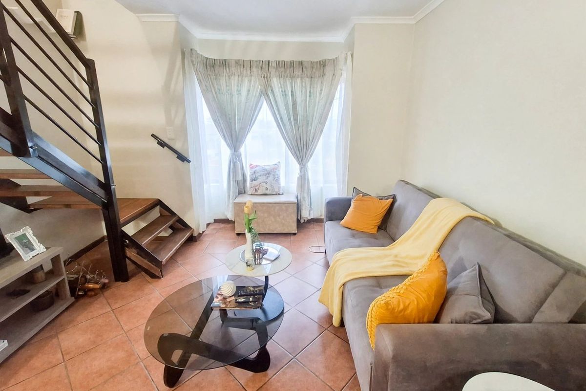 A cozy living room featuring terracotta tiled flooring and an open-plan staircase with a metal handrail, leading to an upper level.