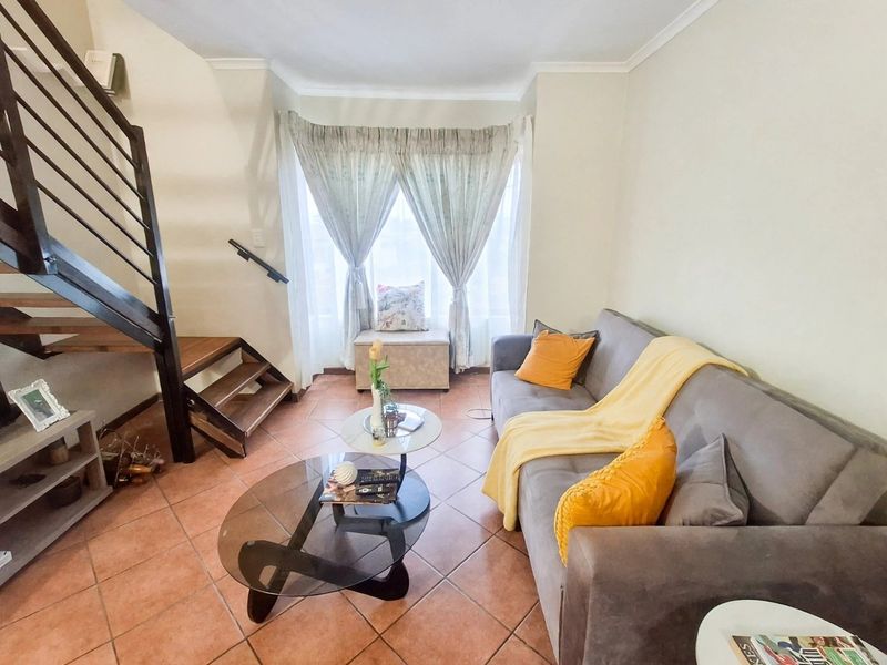 A cozy living room featuring terracotta tiled flooring and an open-plan staircase with a metal handrail, leading to an upper level.
