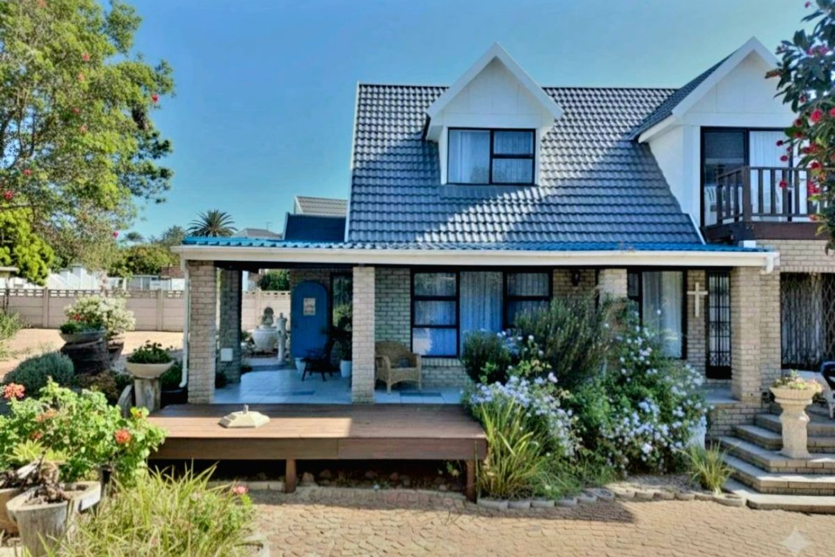 Rear view of a two-story house featuring a tiled roof, covered patio with timber decking, and a balcony overlooking the garden.