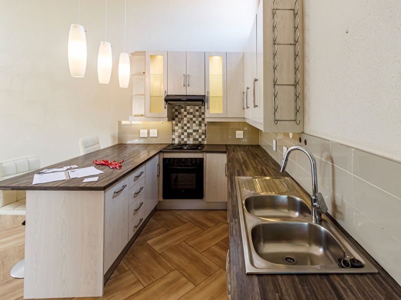 Modern kitchen featuring light wood-finish cabinetry, dark laminate countertops, stainless steel double sink, built-in oven, gas hob, and stylish herringbone flooring.