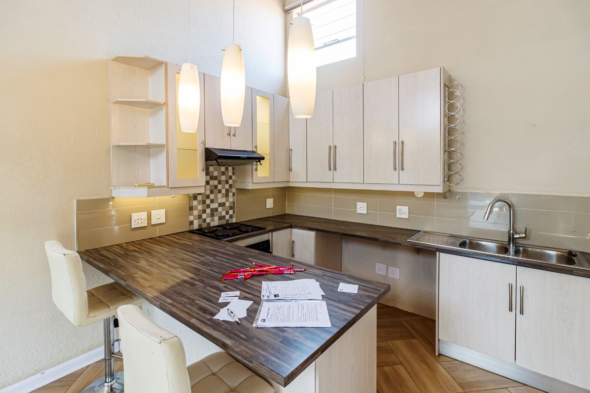 Modern kitchen featuring light wood-finish cabinetry, dark laminate countertops, integrated hob with extractor, and a stainless steel sink with a tiled backsplash.