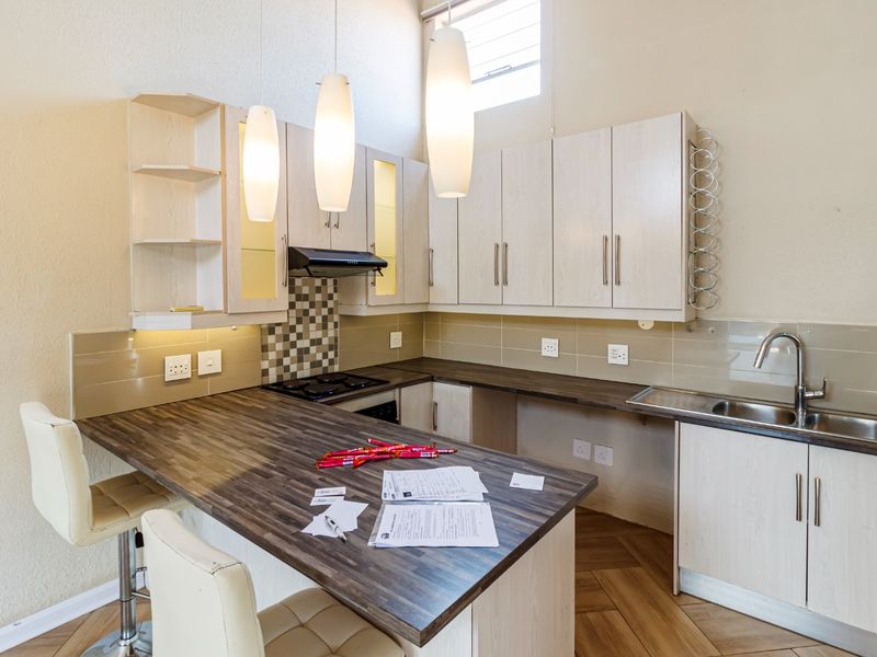 Modern kitchen featuring light wood-finish cabinetry, dark laminate countertops, integrated hob with extractor, and a stainless steel sink with a tiled backsplash.