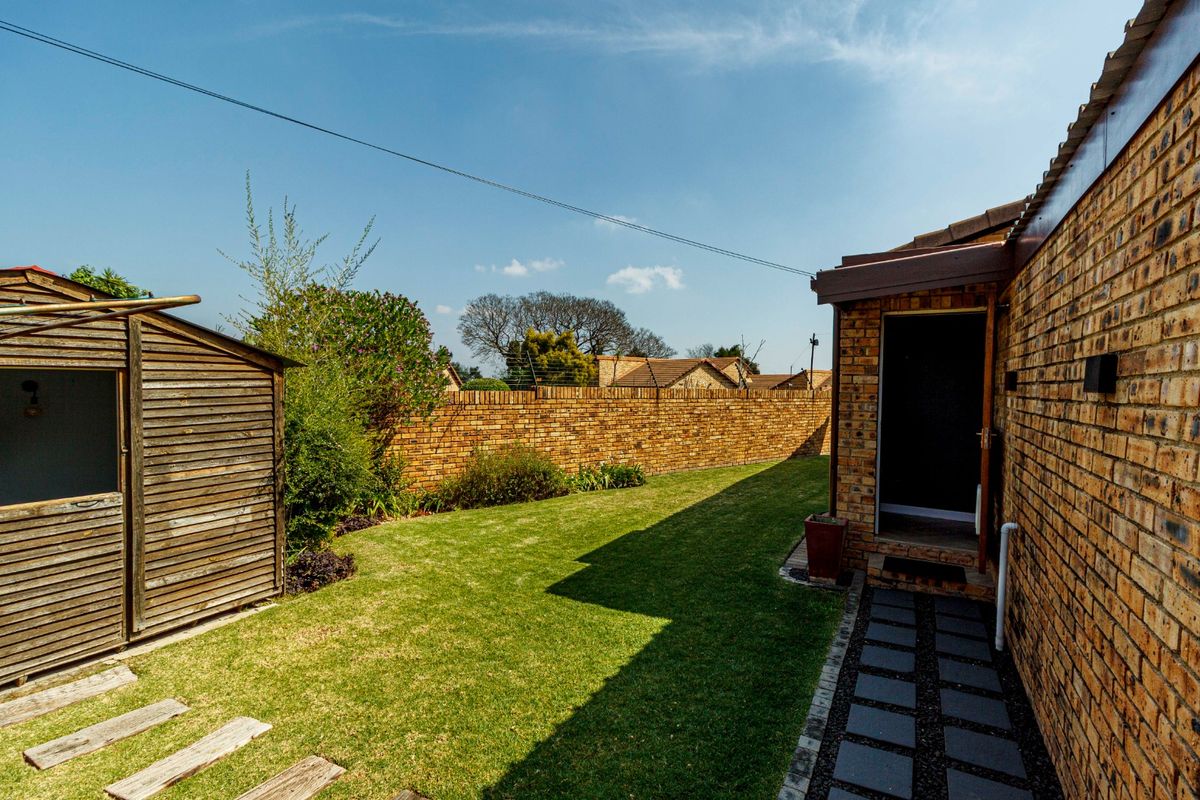 A private rear garden featuring a well-maintained lawn, paved walkway, brick boundary wall with electric fencing, and a wooden storage shed.