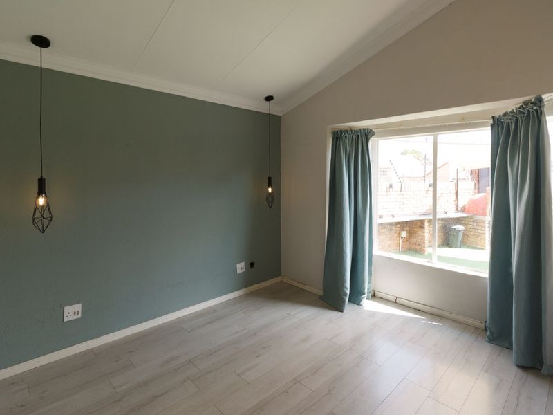A bright, empty bedroom featuring light laminate flooring, a vaulted ceiling, modern pendant lighting, and a large window overlooking the rear garden area.